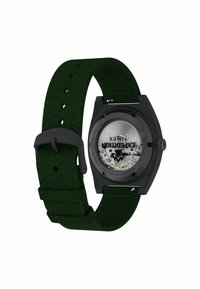 Ceas de mână Timex Expedition cu brățară împletită verde și carcasă neagră, având spate transparent care îmbină mișcarea mecanică.