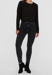 Top negro de manga larga con cuello redondo, combinado con jeans skinny de talle alto negros y botines negros. Textura suave en todo.