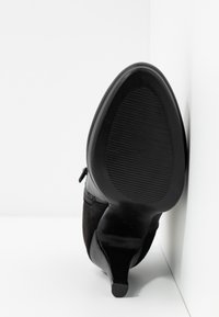 Musta korkokengä, jossa on mokkanahkainen päällinen ja kumipohja. Kengässä on teräväkärkinen kärki ja matala, tyylikäs korko, jossa on teksturoitu pinta.