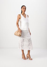Weißes Spitzen-Top und Rock-Set mit fließender Silhouette. Kombiniert mit einer beigen Handtasche und nudefarbenen Blockabsatzsandalen.