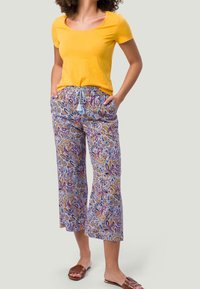 Top amarillo de manga corta, con patrón, pantalones fluidos y ligeros en tonos morados, azules y naranjas, con cintura con cordón y bolsillos abiertos.