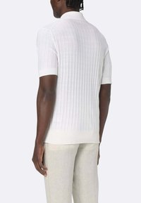 Polo shirt bianco a maniche corte con collare classico e design aderente. Tessuto leggero con una consistenza liscia e bordi a contrasto.