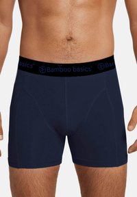 Donkerblauwe bamboe boxershorts met een zwarte elastische tailleband met blauwe logo-tekst. Glad textuur en slim fit ontwerp, knielengte.