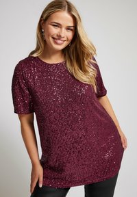 Maroon sequintoppi lyhyillä hihoilla, joka hastee pyöreän kaula-aukon ja teksturoidun kuviolokuvan. Suunnittelu on vartalonmyötäinen ja hieman pidempi pituudeltaan.