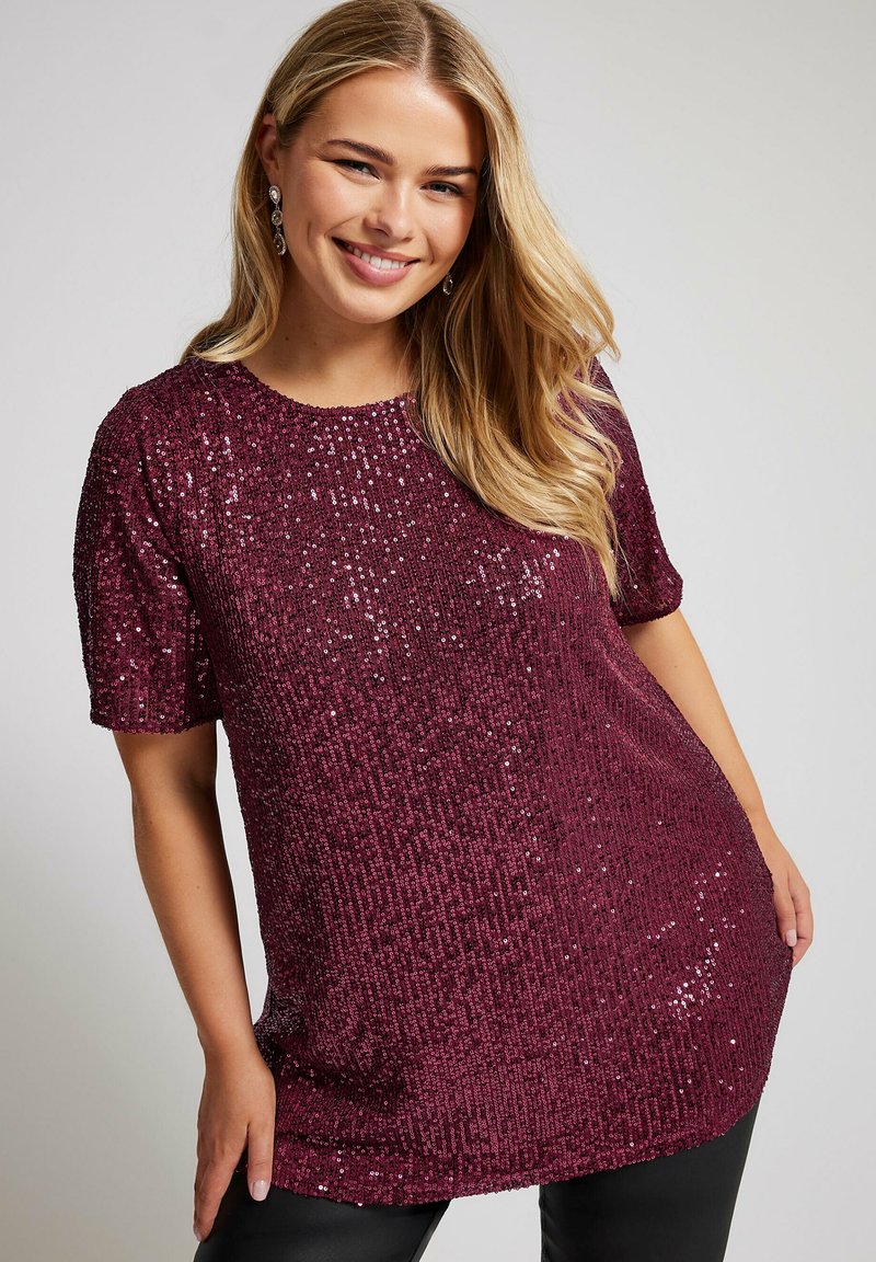 Maroon sequintoppi lyhyillä hihoilla, joka hastee pyöreän kaula-aukon ja teksturoidun kuviolokuvan. Suunnittelu on vartalonmyötäinen ja hieman pidempi pituudeltaan.