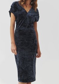 Robe midi en velours bleu marine avec un décolleté en V et des manches courtes, présentant une texture subtile et une silhouette ajustée qui s'évasent jusqu'au genou.