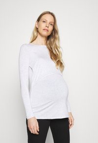 Camisola de maternidade de mangas longas em cinza claro, com um corte relaxado, fabricada em um suave mistura de algodão e com franzidos laterais que acomodam uma barriga em crescimento.