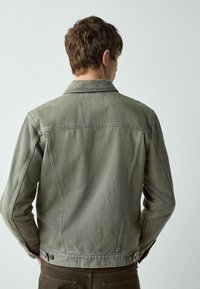 Zaļganas olīvu krāsas džinsa jaka ar apkakli, aizmugures plecu daļu un aproču pogām. Raksturīga fakturēta virsma un smalki šuvju elementi.