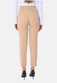 Pantaloni beige su misura con una vestibilità slim, caratterizzati da linee pulite, cuciture verticali e una vita a media altezza, abbinati a tacchi alti neri.