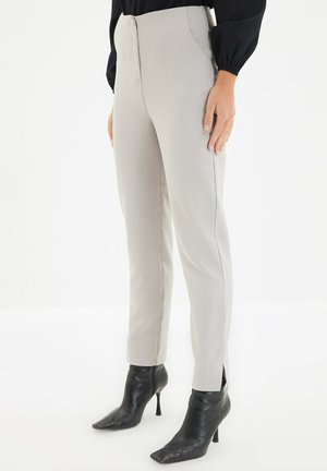 Frau trägt hellbeige gerade Hose mit Seitentaschen und schwarze spitze hochhackige Stiefeletten vor weißem Hintergrund.
