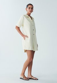 Korte mouwen jumpsuit in lichtgele katoen met een kraaglijn, knoopsluiting aan de voorkant en zijzakken, met een relaxte pasvorm en korte benen.