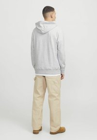 Sudadera gris con capucha, puños acanalados y un dobladillo recto, combinada con pantalones cargo beige y zapatos marrones.