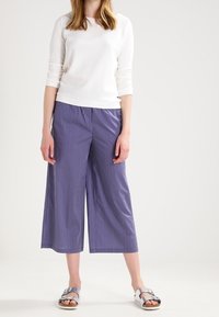 Witte textuur met lange mouwen, gecombineerd met marineblauwe gestreepte culottes en zilveren sandalen, die een ontspannen pasvorm en wijde pijpdesign laten zien.