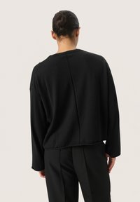 Black oversized sweater with a round neckline, long sleeves, and a cropped hem; smooth texture with a central seam detail at the back.