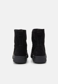 Schwarze Wildleder-Stiefeletten verfügen über eine abgerundete Zehenpartie, eine strukturierte Oberfläche und eine robuste Gummisohle. Kurze Schleife an der Rückseite für ein einfaches Anziehen.