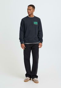 Navyblauwe sweatshirt met de tekst "SUNNY MOOD" in groen. Gecombineerd met een zwarte spijkerbroek en grijze sneakers. Eenvoudig ontwerp en casual pasvorm.