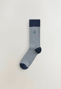 Chaussette rayée bleu marine et blanc avec bord-côte, talon et bout bleu marine, avec un petit emblème d’ancre bleu sur le côté.