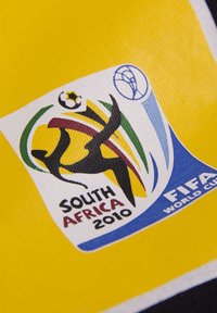 Logo van de FIFA Wereldbeker 2010 in Zuid-Afrika op een gele achtergrond. Bevat een silhouet van een speler, kleurrijke krullen, en de tekst "ZUID-AFRIKA 2010."