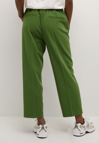 Pantaloni larghi verdi con una texture liscia, vita elasticizzata e due tasche posteriori. Abbinati a scarpe da ginnastica grigie e bianche.