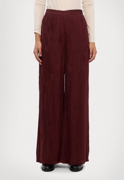 Pantalons à jambe large en velours côtelé bordeaux. Dotés d'une texture à côtes verticales et d'une taille haute. Fabriqués à partir d'un tissu doux, assortis de chaussures noires.