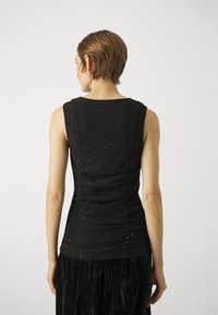 Sorte ermeløs topp med teksturert overflate, som har subtile paljetter, rund halsutskjæring, og samlet detailing på baksiden.