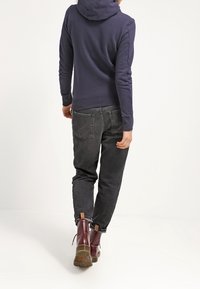 Mörkblå hoodie med huva, i kombination med svarta jeans. Bruna läderankelboots med texturerad sula och synlig sömnad.