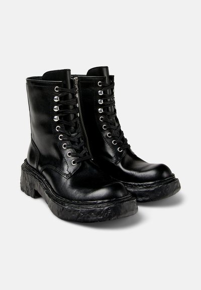 Black leather ankle boots with a thick, textured platform sole, silver eyelets, and laces, featuring a side zipper for easy wear.