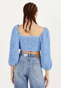 Modrý krácený top s texturovanou, volánkovou tkaninou a nabíranými rukávy. V kombinaci s světle modrými džíny s vysokým pasem a páskem s kovovými detaily.