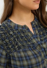 Blue and green plaid blouse featuring textured, ruffled accent at the shoulders, with a rounded collar and button-down front.