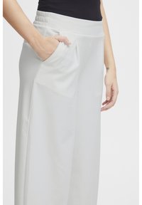 Helle graue, weit geschnittene Hose aus einem weichen, strukturierten Stoff, mit einem gerafften Bund und seitlichen Taschen für Funktionalität.