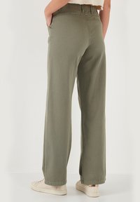Weite olivgrüne Hosen aus weichem Baumwollstoff mit einem elastischen Bund und seitlichen Taschen. Sie sind gerade geschnitten und haben minimale Nähte.