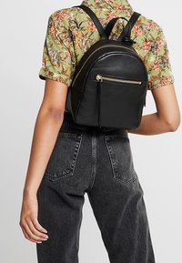 Schwarzer Leder-Rucksack mit runder Form. Verfügt über eine vordere Reißverschlusstasche, verstellbare Träger und eine glatte Textur. Ideal für den Freizeitgebrauch.