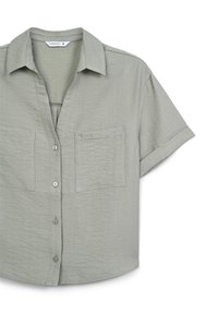 Camicia a maniche corte con colletto di colore verde chiaro, caratterizzata da un tessuto testurizzato, due tasche sul petto e chiusura frontale con bottoni.