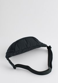 Sac banane noir matelassé avec sangle réglable et boucle en plastique, présenté sur un fond clair uni.