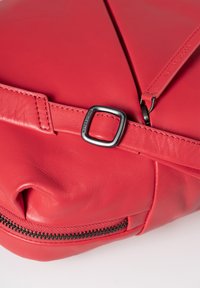 Rode leren tas met een gestructureerde afwerking, voorzien van een ritsluiting, een band met een metalen gesp en minimalistische designelementen.
