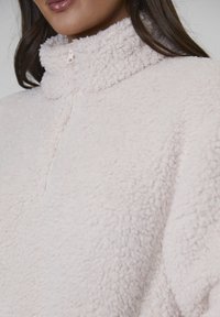 Ljusrosa fleecepullover med hög krage och halvdragkedja. Mjuk, texturerad material med en mysig look.