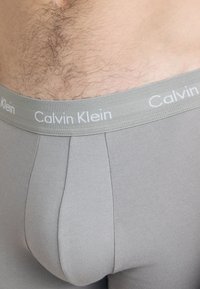 Grå bomullsboxere med en tykk elastisk linning som har hvit "Calvin Klein"-merking og et glatt, tettsittende design.