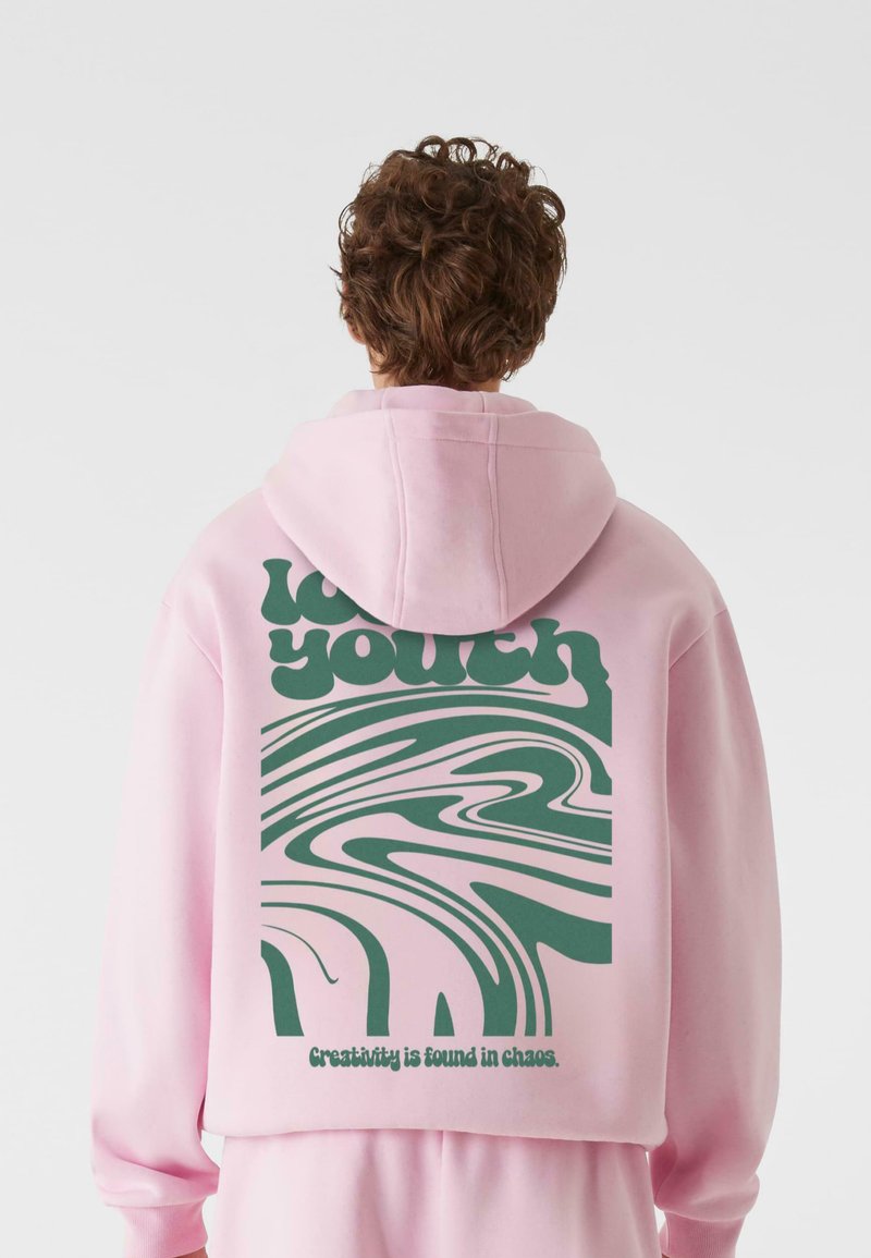 Sweat à capuche rose avec un graphisme vert présentant des lignes sinueuses et le texte "love youth". Le dos comporte la phrase "La créativité se trouve dans le chaos."