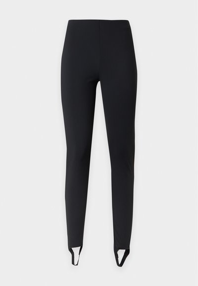 Leggings noirs slim fit avec brides étriers aux chevilles, présentés sur un fond clair uni.