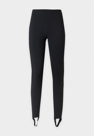 Leggings noirs slim fit avec brides étriers aux chevilles, présentés sur un fond clair uni.
