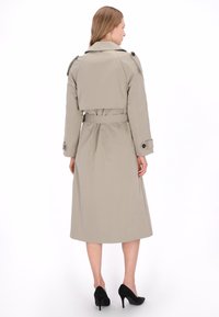 Beige trenchcoat met een getailleerde taille, lange mouwen, met knopen afgewerkte manchetten en een ontwerp met ceintuur. Glad, waterafstotend materiaal, tot op de knie.