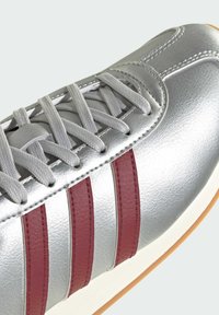 Silver leather sneaker with textured finish, featuring three maroon stripes, grey laces, and a rubber sole. Clean and simple design.