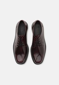 Scarpe da uomo in pelle bordeaux con finitura lucida, design allacciato e suola in gomma nera. Presentano accenti cuciti lungo la tomaia.