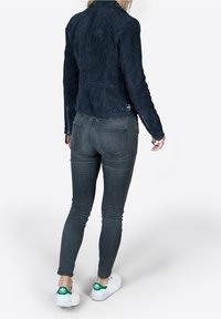 Navy suede jacket with a fitted design and back detail, paired with dark gray skinny jeans and white sneakers featuring green accents.