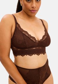 Brun spets-bustier med mjuka kupor och vågiga kanter, kombinerad med höga trosor som har blomster spetsdetaljer och genomskinliga paneler.