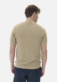 Krátký béžový polo shirt s krátkými rukávy, texturovaným vzorem rybí kosti, žebrovaným límcem a lemem, přiléhavým střihem a bočními rozparky.