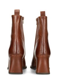 Par de botines de cuero marrón con tacones de bloque y cremalleras laterales, vistos desde atrás sobre un fondo blanco.