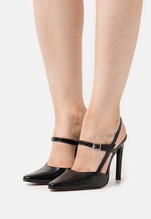 Chaussures noires en cuir à talons aiguilles avec des pointes fines, des brides de cheville fines et une finition brillante. Présente un talon aiguille et un design minimaliste.