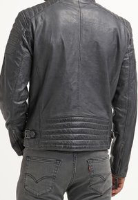 Sort lædermotorcykeljakke med ribbet skulderdetaljer og spændeaccenter; har et tætsiddende design og glat tekstur.