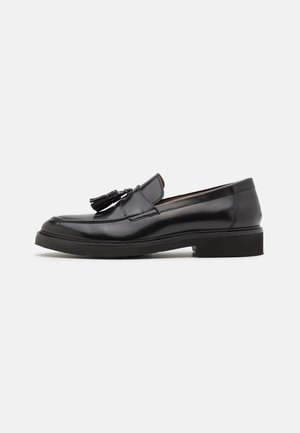 Mocassins en cuir noir avec des détails en franges, bout rond et semelle texturée. Présente une finition lisse et un design minimaliste.